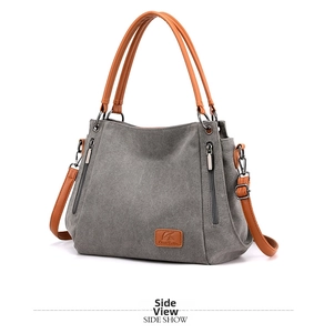 Side view of a grey canvas crossbody bag with brown leather handles and side zippers