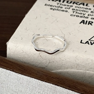 Detailed close-up of a minimalist 925 sterling silver wave ring on a textured surface