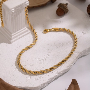Détail du collier chaîne torsadée bicolore or et argent sur texture de pierre blanche