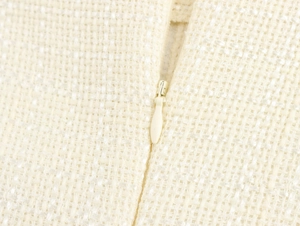 Detailopname van de witte tweed stofstructuur en de verborgen onzichtbare rits op de jurk