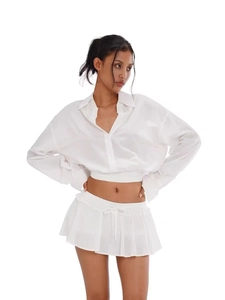 Detail of white long sleeve cropped shirt and pleated mini skirt with waist tie details