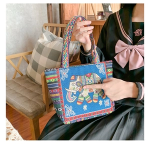 Close-up of ethnic embroidered handbag with colorful elephant pattern on blue fabric