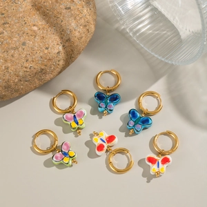 Golden hoop earrings with colorful hand-painted butterfly charms on stone and glass background
