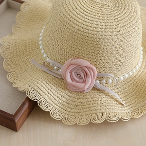 Straw sun hat for girls with pink rose flower, pearls and wavy brim on wood background