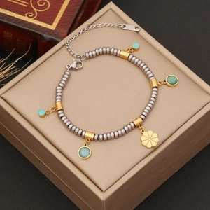 Stainless steel beaded bracelet with gold flower pendant and turquoise charms on a box
