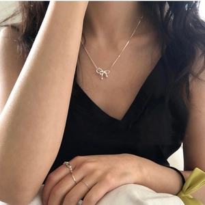 Close-up of elegant S925 silver bow pendant necklace and pearl ring worn by a model