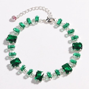 Detailed view of silver chain bracelet with emerald green zircon gems and a pink drop charm