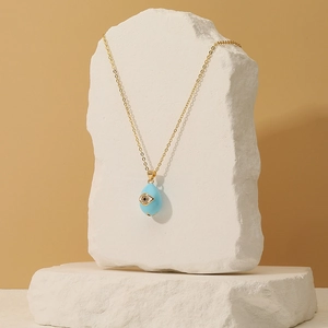 Detail of light blue teardrop evil eye pendant on a gold chain over white stone decor