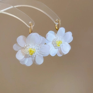 Macro detail of floral earrings with white sequins petals and gold zircon ear buckles