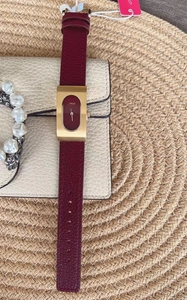 Detail of elegant rectangular gold watch with red leather strap on woven texture mat