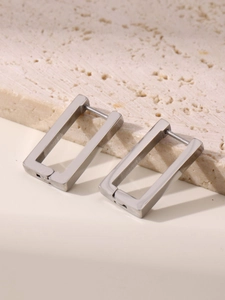 Detail of silver rectangular geometric hoop earrings on a textured stone surface