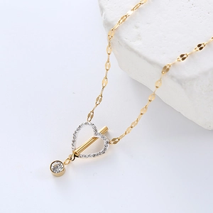 Golden heart necklace with diamonds and OT buckle on a minimalist white stone surface