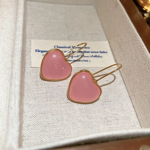 Pink resin heart earrings with gold trim and hooks shown on jewelry display box