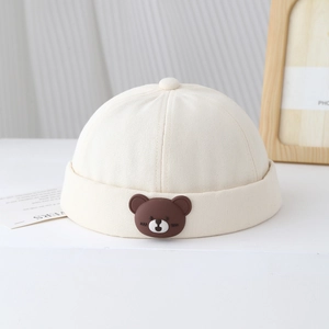 Détail d'un bonnet docker beige avec un joli écusson d'ours en silicone pour les tout-petits