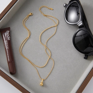Detail of double-layer gold snake chain and bead necklace with a minimalist bean pendant