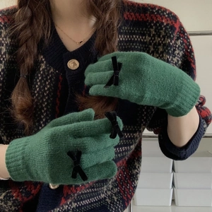Detailed close-up of green knitted gloves with black bow accents and ribbed cuffs