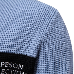 Close-up of light blue waffle knit texture and black embroidered brand tag on the sleeve