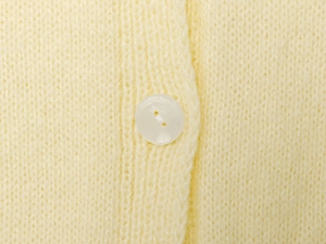 Macro view of a white resin button on a light yellow fine knitted cardigan texture