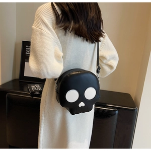 Detail view of a black skull crossbody bag with white heart nose on a white knit sweater