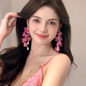 Détail de boucles d'oreilles à fleurs roses et pampilles de perles portées par un modèle
