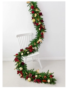 Detail of a 2.7m velvet ball Christmas garland with bows draped over a white wooden chair