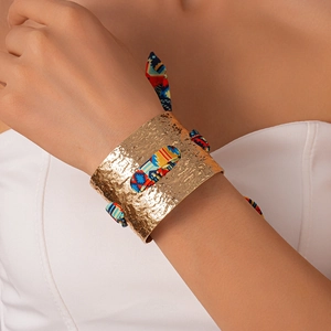 Dettaglio del bracciale rigido dorato martellato con inserto in tessuto boho annodato