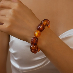Detail of chunky amber acrylic beaded bracelet on wrist over white silk fabric