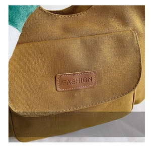 Close-up of mustard yellow canvas tote bag showing the exterior pocket and fashion label