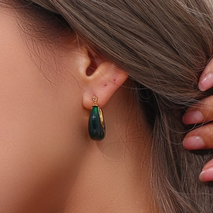 Close-up of elegant gold hoop earrings with dark green teardrop gemstone pendants