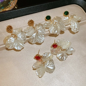 Detail of floral earrings with pearl petals and colorful gems on a beige tray