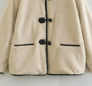 Détail de la veste en peluche crème avec bordures contrastées noires et boutons brandebourg