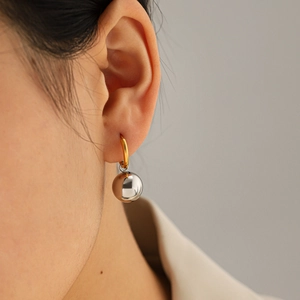 Close-up of modern two-tone steel hoop earrings with a polished silver ball drop on model