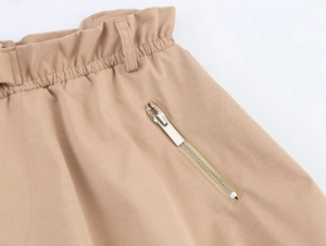 Dettaglio degli shorts a sbuffo kaki con vita elastica, passanti e tasca con zip in metallo
