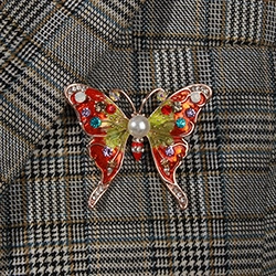 Detail of luxury dragonfly brooch with red enamel wings and white pearl on grey plaid suit