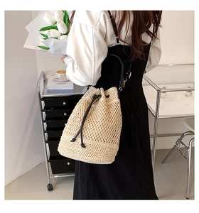 Back view of model carrying a beige woven straw bucket bag with black drawstring closure