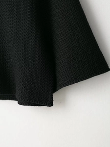 Close-up of black knit fabric with granular texture and detailed hemline craftsmanship