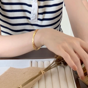 Detailed view of irregular hammered gold bangle on a female wrist with aesthetic decor