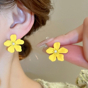 Detail of a bright yellow floral earring with pearl center on ear and hand view