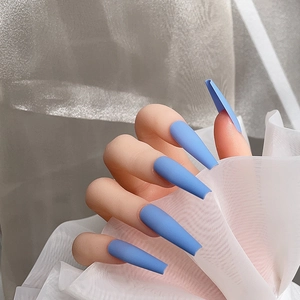 Détail de faux ongles longs ballerine bleu mat portés sur une main avec du tissu
