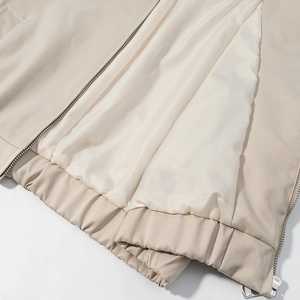 Detail of cream jacket featuring smooth white lining, metal zipper and elastic ribbed hem