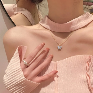 Detail of a gold butterfly pendant necklace and floral pearl ring on a model in pink