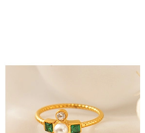 Macro detail of gold rope ring with emerald green gems and white pearl center