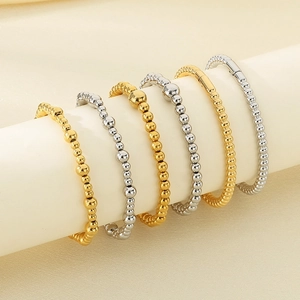 Detailed view of 18K gold and silver plated stainless steel beaded bracelets on a display stand