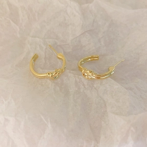 Detailed macro view of golden knot earrings on a textured white background paper