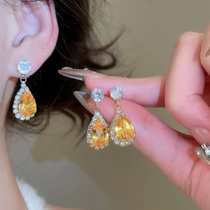 Macro view of teardrop earrings featuring yellow zircon stones and gold-plated setting