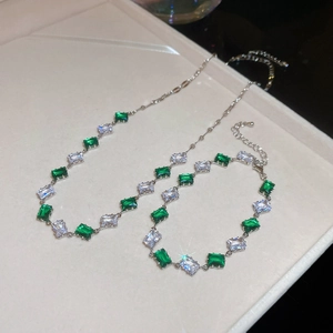 Detailed macro of silver necklace and bracelet set with green and clear square zircons