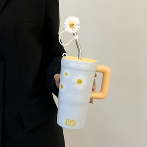 Detail of light blue ceramic mug with yellow handle, daisy pattern and metal straw