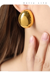 Close-up of elegant oversized golden egg-shaped earrings with mirror-like polished finish