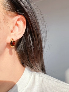 Close-up of elegant gold hoop earring with a large dark red zircon stone worn on model