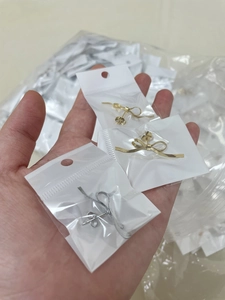 Close-up of bowknot ribbon stud earrings in gold and silver finish being held by hand